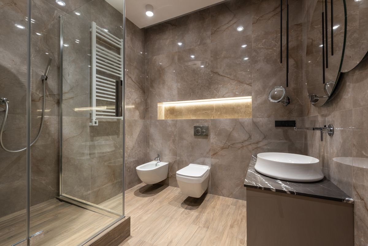 Stone-Finish Bathroom with Glass Shower and Lit Wall Niche
